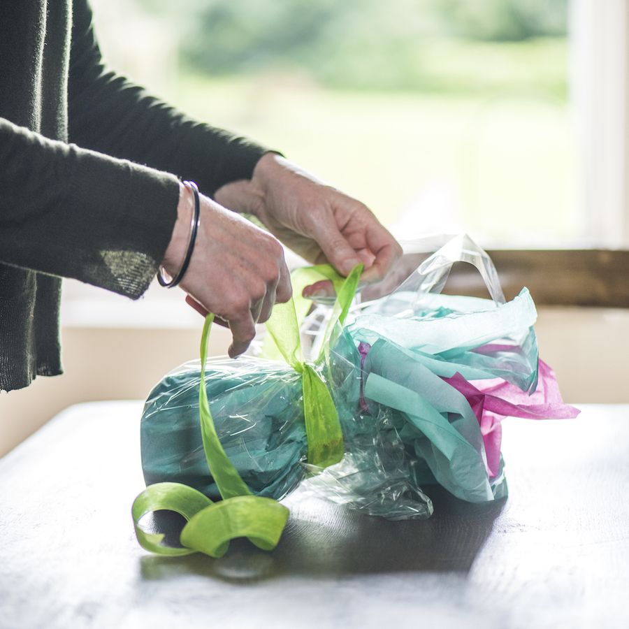 hands wrapping a present using tissue paper, cellophane and ribbon