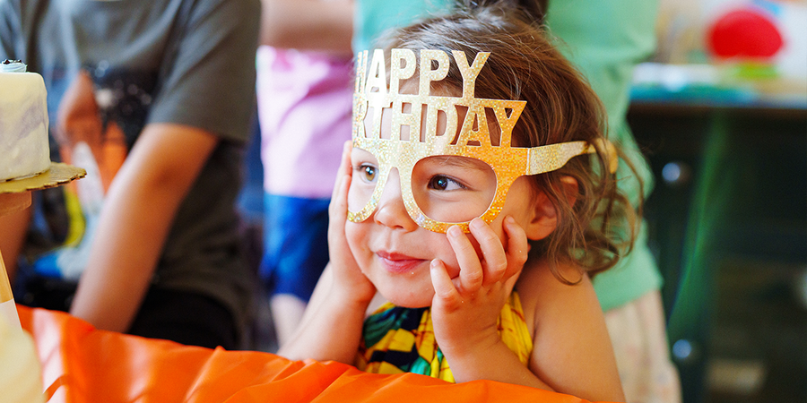 A young girl wearing colourful Happy Birthday party glasses, looking for birthday gift ideas and birthday presents from Photobox.