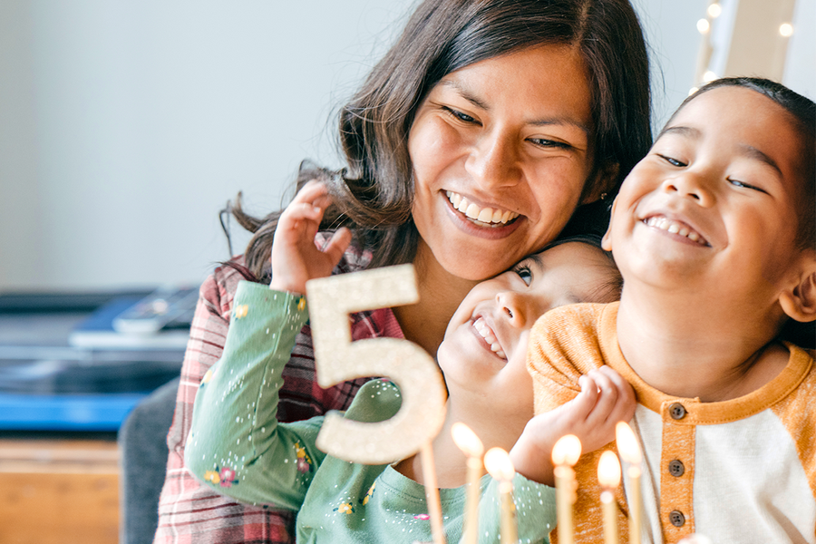 A mother and two children smiling next to a 5th birthday cake, illustrating birthday gifts for mum and birthday present ideas from Photobox.