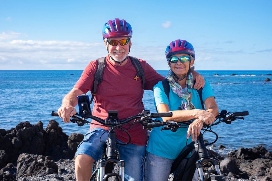 An older couple posing with their bikes in front of the sea, demonstrating an American shot and cinematic framing techniques for photography with Photobox.