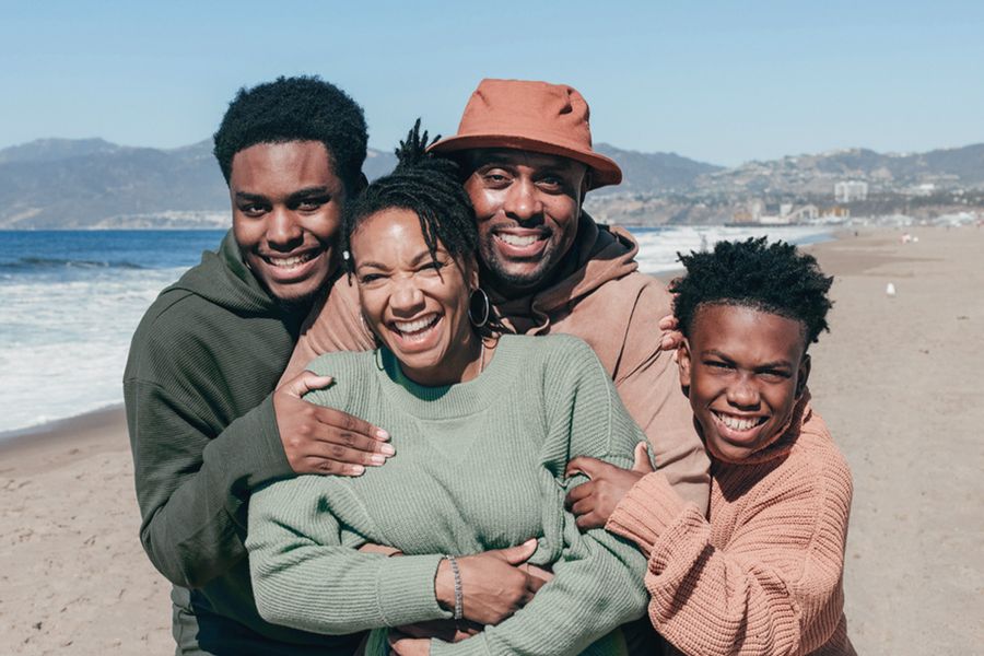 A medium shot of a family of four embracing and smiling on the beach, highlighting the waist-up framing and natural types of shots in photography with Photobox.