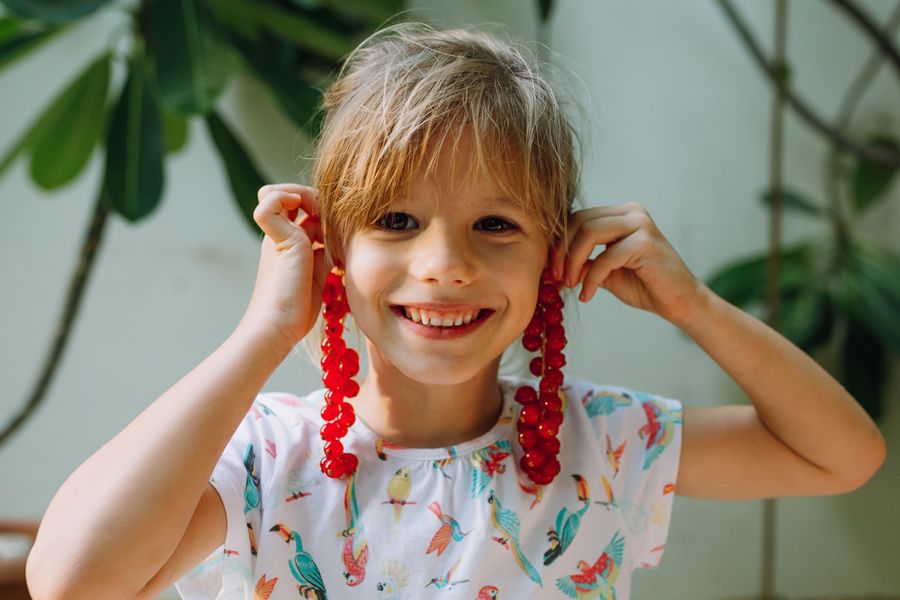 A medium close-up of a little girl smiling while holding fruit to her ears like earrings, demonstrating intimate framing and portrait photography tips with Photobox.