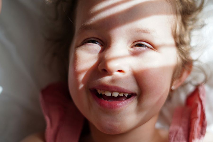 An extreme close-up of a little girl smiling with sunlight and shadows across her face, illustrating cinematic portraiture and types of photography shots with Photobox.