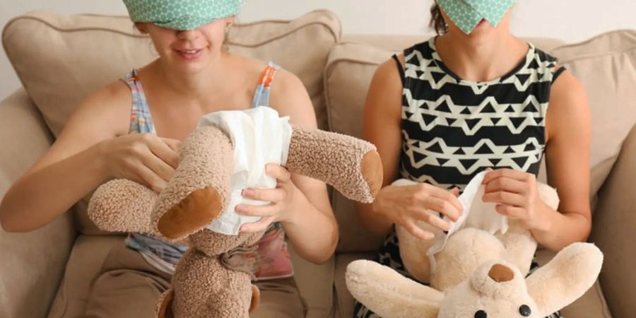 Two people competing to dress baby dolls at a co-ed baby shower with nappies and baby clothes, showing a fun baby shower game from Photobox.
