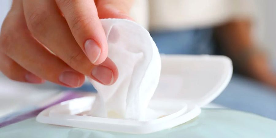 A guest at a baby shower trying to pull a single nappy wipe from a pack with one hand, showing the 