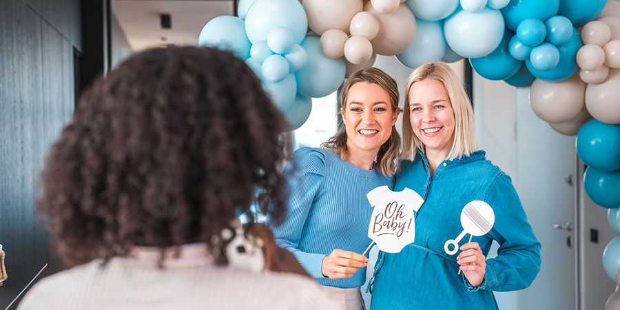 A fun group photo of guests at a baby shower photo booth dressed in baby accessories and holding prizes, capturing the best baby shower games from Photobox.