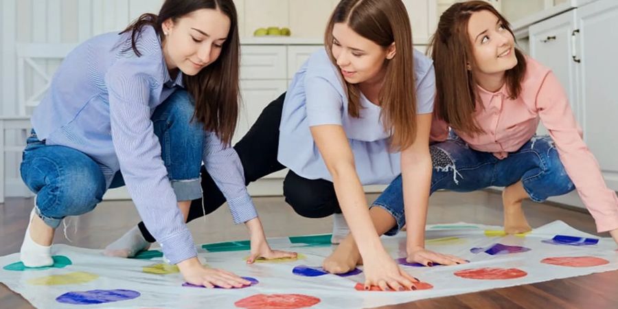 Women playing Twister at a baby shower with pillows under their shirts, showing funny baby shower games for boys or girls from Photobox.