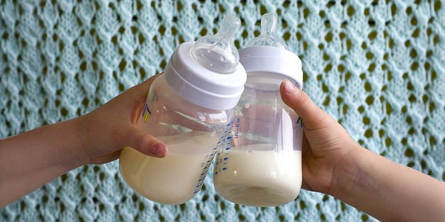 A group of men and women competing in a baby bottle drinking race at a baby shower, illustrating fun baby shower games for men and women from Photobox.