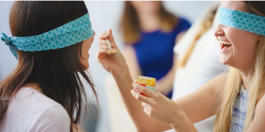 A blindfolded mum-to-be feeding her partner during a hilarious baby shower game, showing fun baby shower activities and baby shower ideas from Photobox.