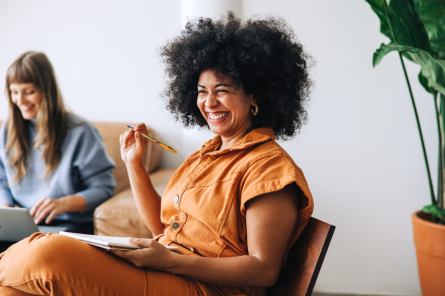 A woman smiling with a pen and a notebook while planning the budget and guest list for a hen party with Photobox.