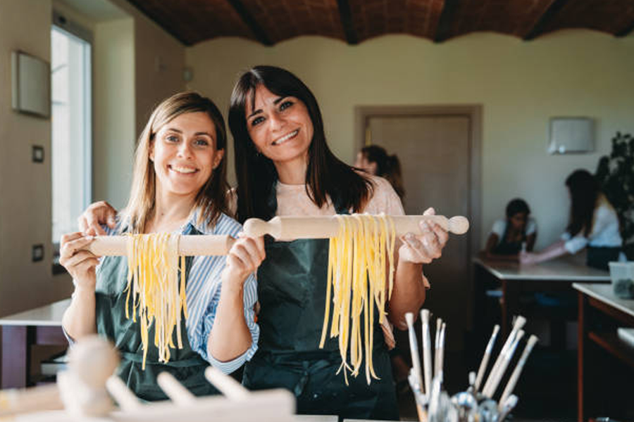 Two women smiling at a pasta making workshop, a fun cooking activity idea for a hen party with Photobox.