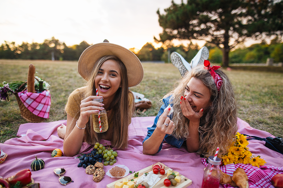 Two women surrounded by food on a picnic blanket, a perfect idea for a picnic photo shoot and hen party ideas from Photobox.