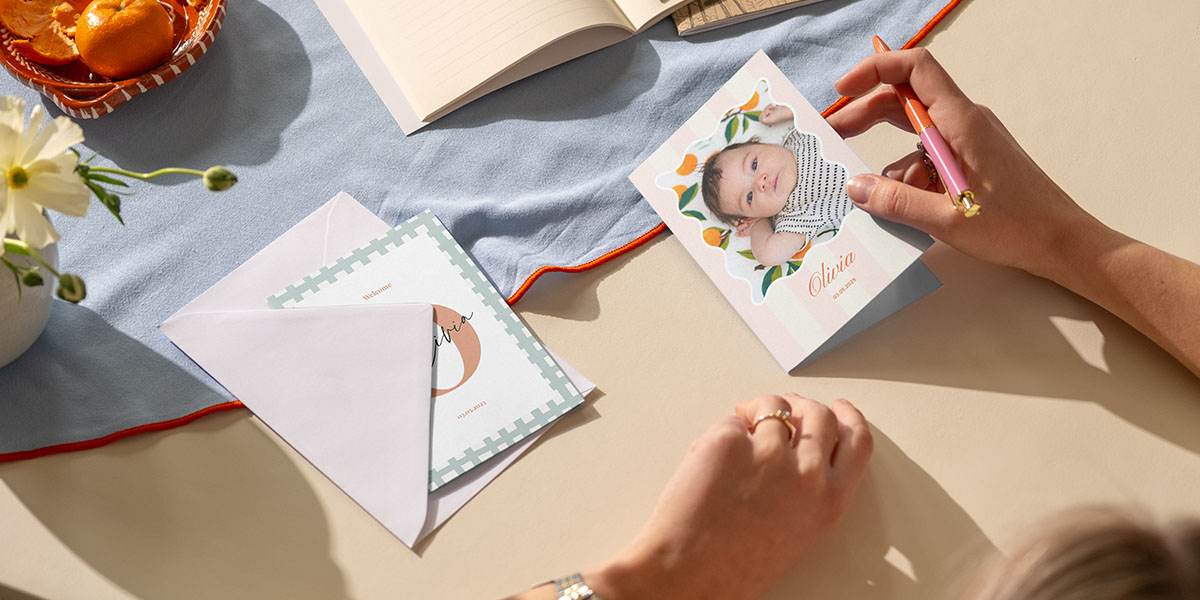 A woman writing a card for a newborn baby girl, looking for inspiration on what to write inside a newborn card with Photobox.