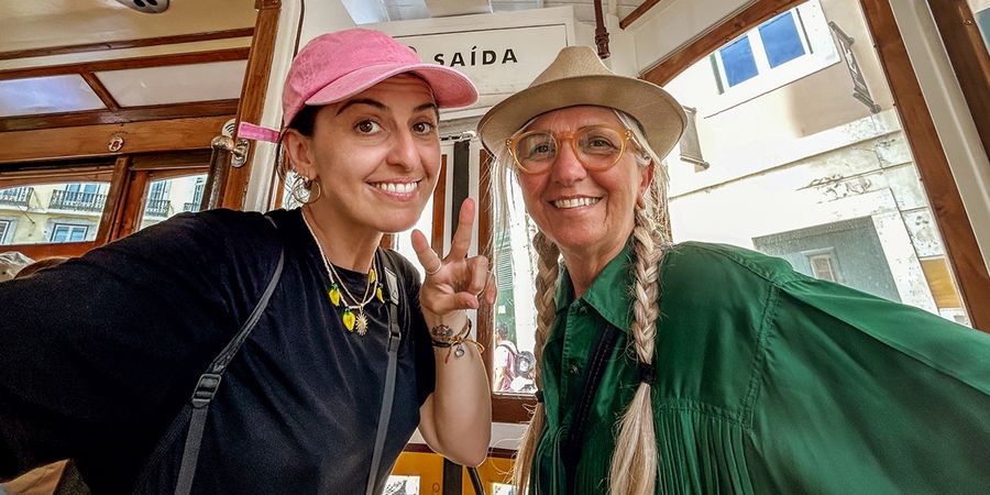A smiling mother and adult daughter sitting together on a tram with the daughter making a peace sign, representing the joy of mother's day gifts and heartfelt card messages with Photobox.