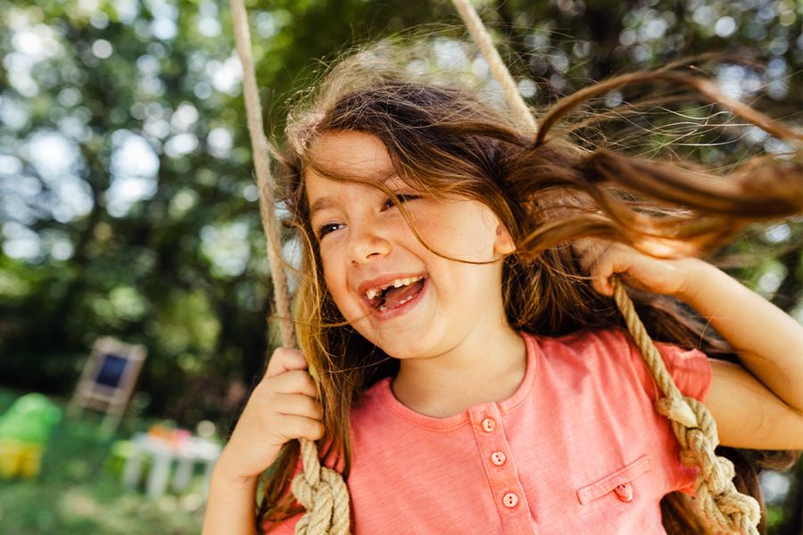 A little girl smiling on a swing, inspiring Photobox spring photography tips and dynamic spring photo ideas that capture movement and joy outdoors.
