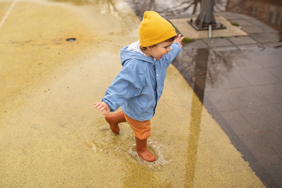 A little boy playing in puddles, inspiring Photobox spring photography tips for capturing rainy spring moments, reflections and bright colours on a wet day.