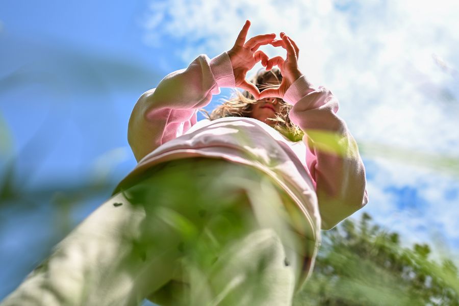A little girl making a heart shape with her fingers, inspiring Photobox spring photography ideas that use perspective, framing and creative angles to capture special moments.