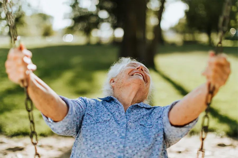 A smiling older man on a swing outside on a sunny spring day, inspiring Photobox spring photography ideas and the joy of capturing the spring season.