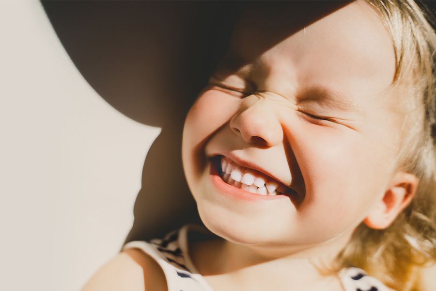 A sunny portrait of a smiling little girl with spring sun on her face and soft shadows in the background, inspiring Photobox spring photography ideas and golden hour portraits full of warm light.