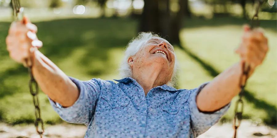 A smiling older man on a swing outside on a sunny spring day, inspiring Photobox spring photography ideas and the joy of capturing the spring season.