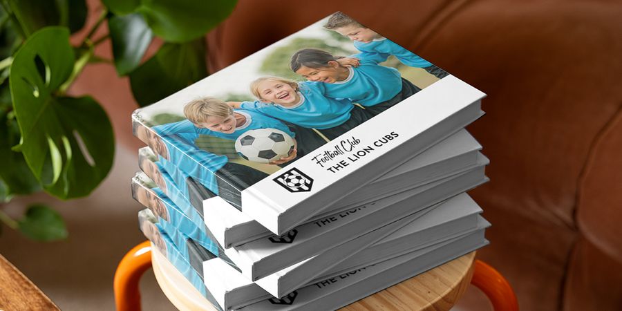 A Photobox school photo book showing a sports team of children in football kits embracing and holding a football, inspiring school yearbooks, sports team photo books and school photo book ideas.