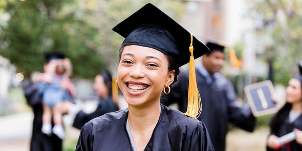 A smiling female graduate standing outside in a cap and gown, inspiring Photobox graduation gift ideas and personalised graduation gifts.
