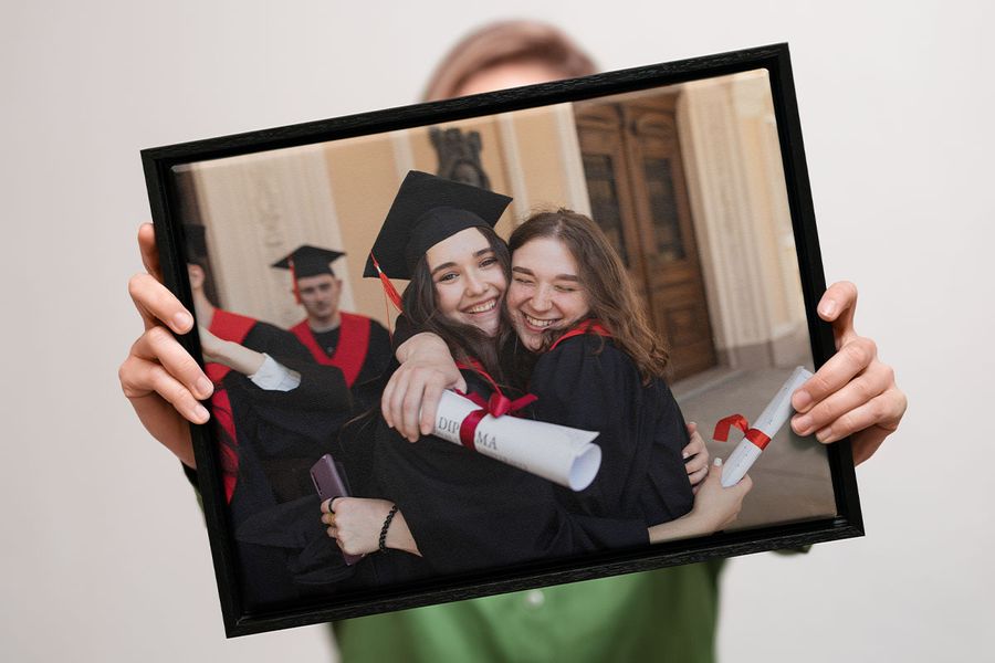 Someone holding Photobox graduation wall art on canvas showing two smiling graduates embracing and holding their diplomas, inspiring personalised graduation gifts and graduation wall art ideas.