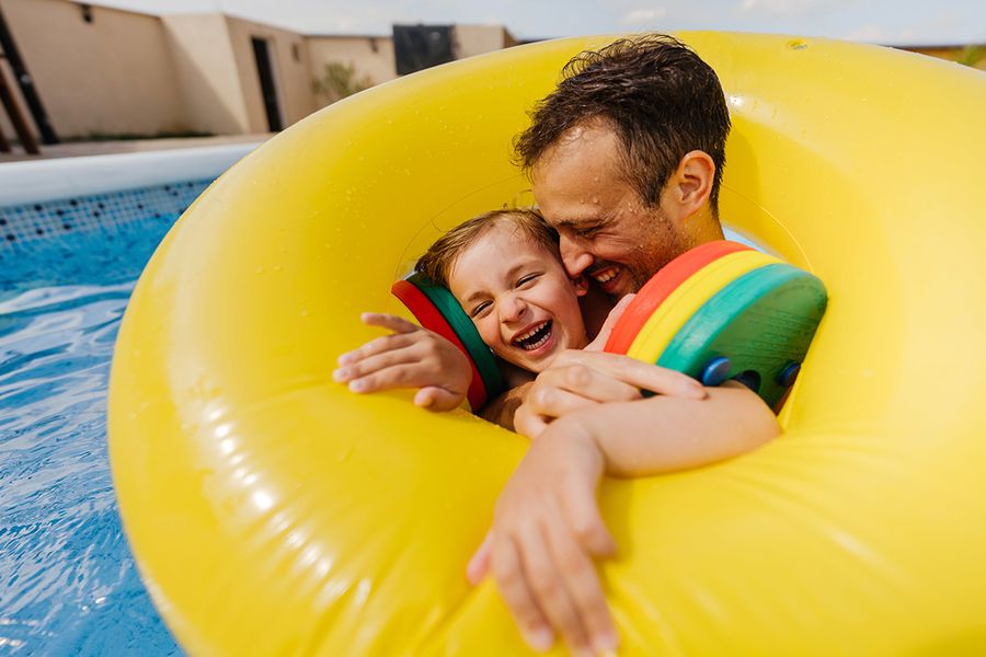 A father and child floating in a rubber ring in a swimming pool on holiday, ideal for summer photo captions for social media from Photobox.