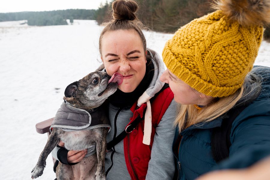 Two smiling women in the snow, one being licked by her pug, finding what to write in a Valentine's Day caption about your pet to go with Valentine's day ideas from Photobox.