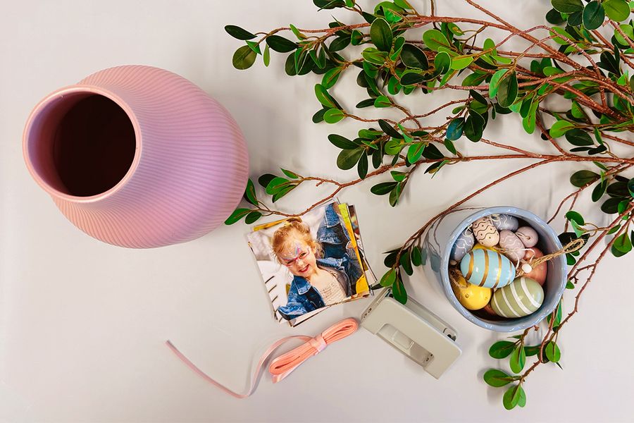 A collection of materials for a DIY Easter centerpiece including a vase, photo prints, branches, twine, a hole punch, and egg decorations, perfect for Easter crafts for kids with Photobox.