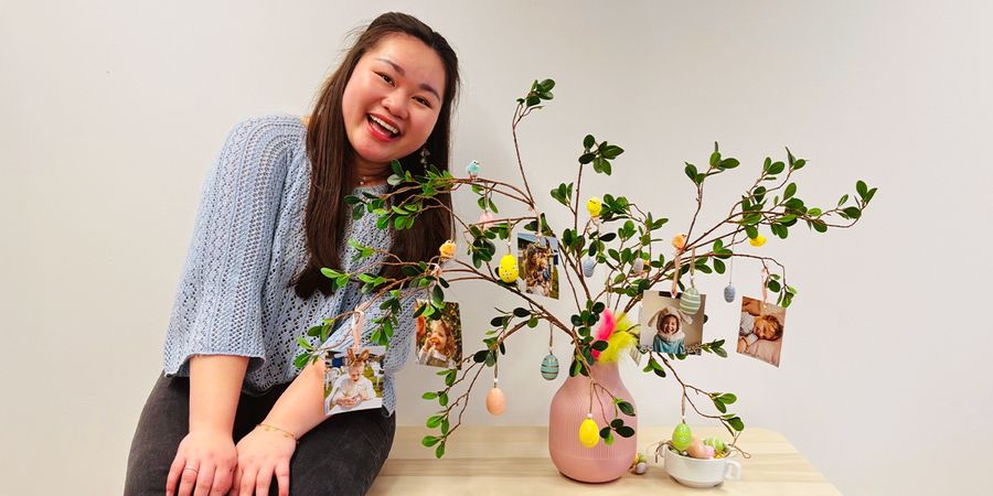 Vannie, social marketing specialist at Photobox, standing next to a completed DIY Easter centerpiece featuring a tree in a vase with personalised photo prints hanging from the branches.