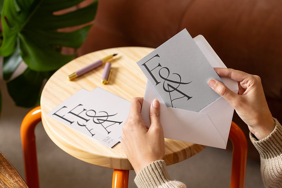 A classic Photobox personalised wedding invitation on a table as someone places the invite into an envelope, inspiring elegant wedding invitation wording and classic wedding card messages.