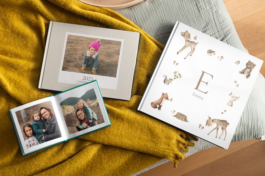 Photobox photo books on a blanket, including a baby photo book and a year in review photo album, with an open photo print box showing family snaps of a mother and daughter.