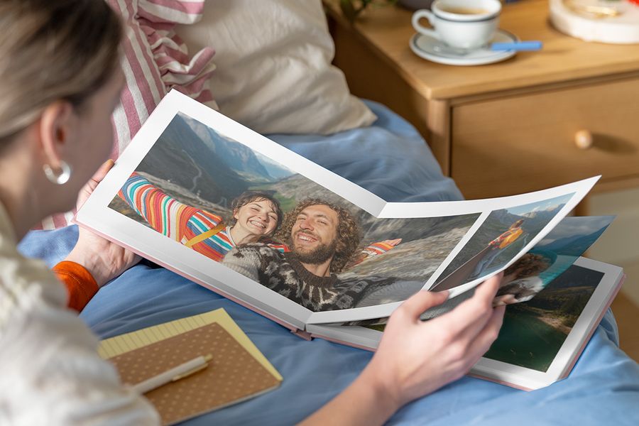 Photobox photo book inspiration: a woman looking at an open personalised photo book with a double-page spread of a couple in a mountainous landscape.