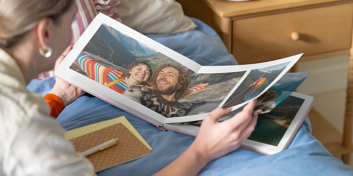 Photobox photo book inspiration: a woman looking at an open personalised photo book with a double-page spread of a couple in a mountainous landscape.