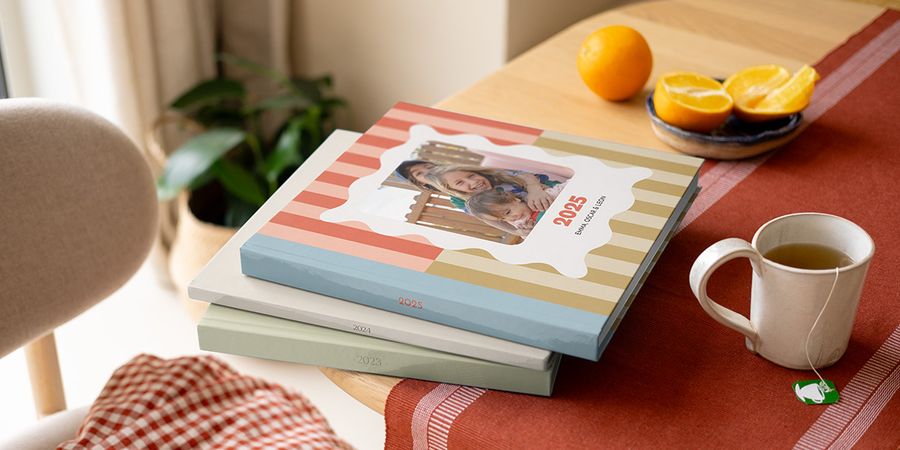 A stack of colourful, patterned Photobox yearly photo books and annual photo albums with varying designs, sitting on a coffee table.
