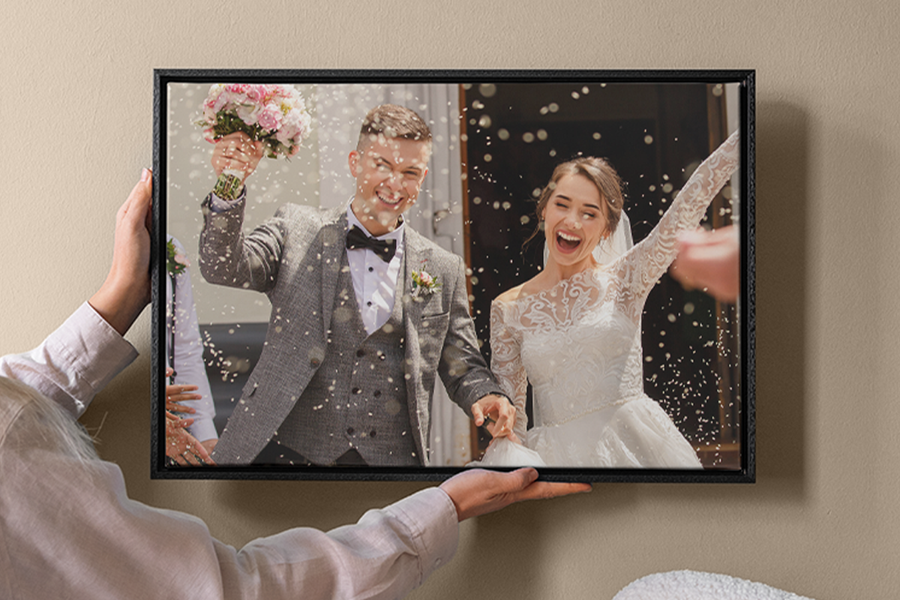A woman placing a custom wedding canvas from Photobox on a wall, showcasing a bride and groom smiling under falling confetti.