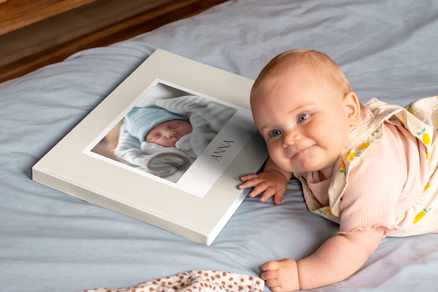 Smiling baby lying beside a 1st year photo album