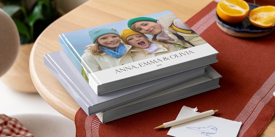 A selection of Photobox photo books on a table with a pen, featuring siblings on the cover and providing inspiration for what to write in a photo album with family photo album captions.