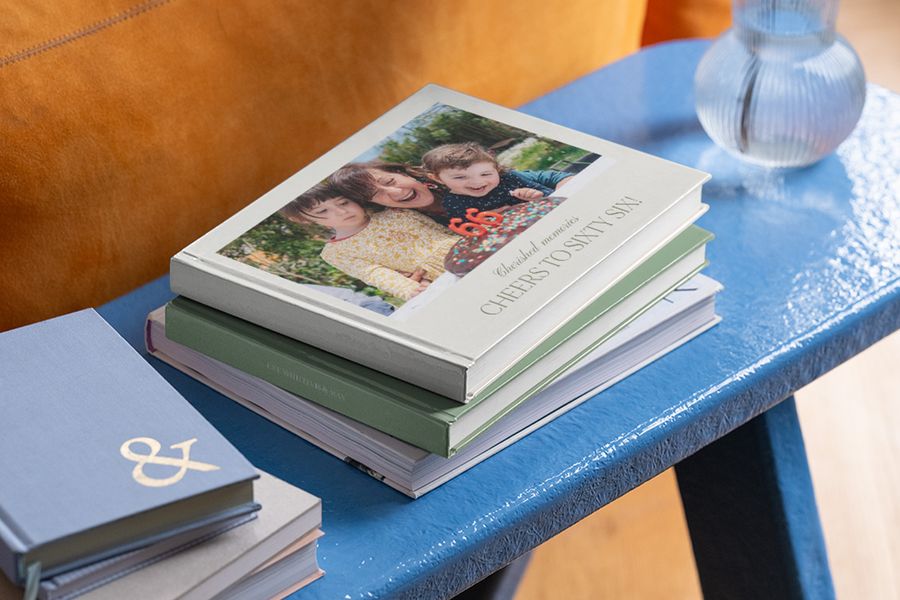 A stack of birthday photobooks on a table, with the top 60th birthday photo book or 60th birthday memory book featuring a grandmother and grandchildren on the cover from Photobox.