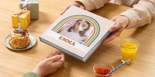 A birthday photo book for Emma is passed across a table with a cake and a present, showing how to create a photo album birthday gift or birthday photobooks with Photobox.