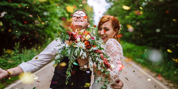 A happy couple celebrating outside on their wedding day while being covered in falling confetti, illustrating the 2026 wedding trends and a move toward personal ceremonies with Photobox.