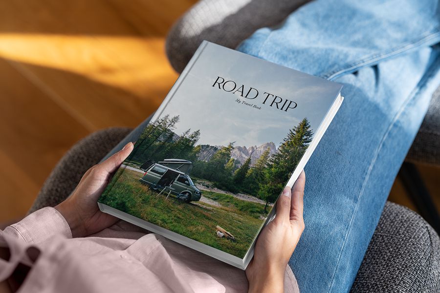 A Photobox coffee table photo book called Road Trip resting in someone’s lap, with a forest landscape and camper van on the cover, inspiring a travel coffee table photo book.