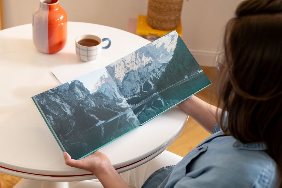 An open Photobox coffee table photo book showing a double-page spread of a mountainous lake landscape, inspiring a photography coffee table book and a custom coffee table photo book.