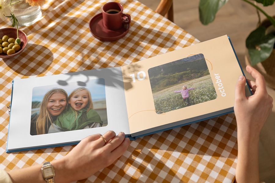 An open Photobox coffee table photo book showing a mother and daughter on one page and a little girl frolicking in a field of flowers on the other, inspiring a personalised coffee table photo book and a family coffee table photo album.