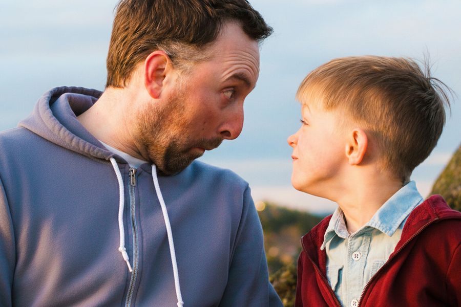 A father and son pull funny faces while looking at each other, inspiring funny Father’s Day cards and what to write in a Father’s Day card.