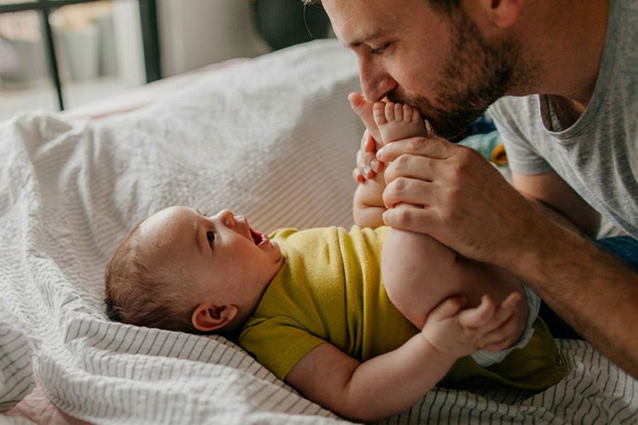 A father kisses his baby’s feet, inspiring a first Father’s Day card, happy first Father’s Day wishes and meaningful Father’s Day messages.