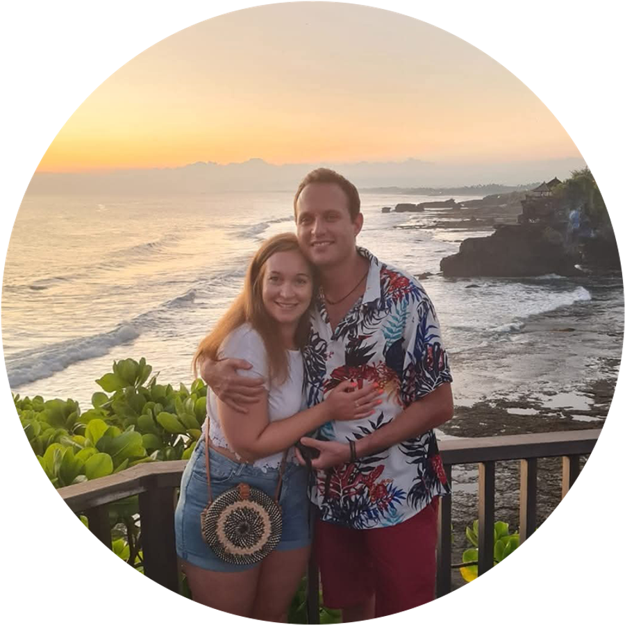 Claudia and her husband smile together beside a beautiful Bali sunset, illustrating her romantic proposal story.